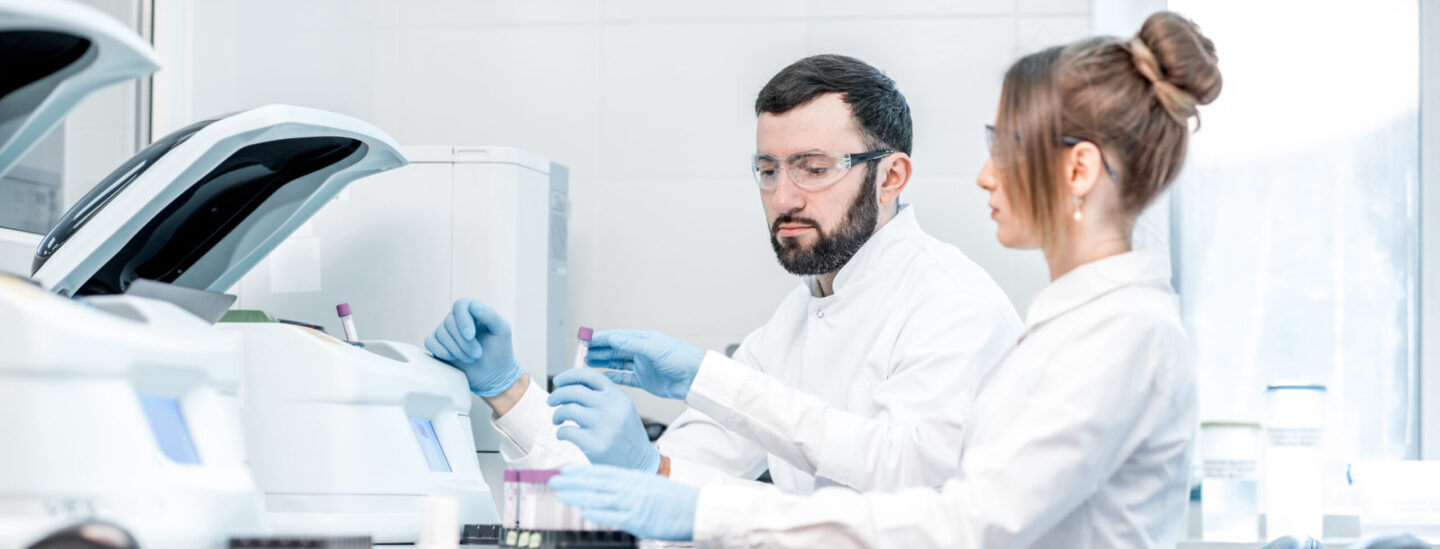 Laboratory assistants making analysis with test tubes and analyzer machines sitting at the modern laboratory